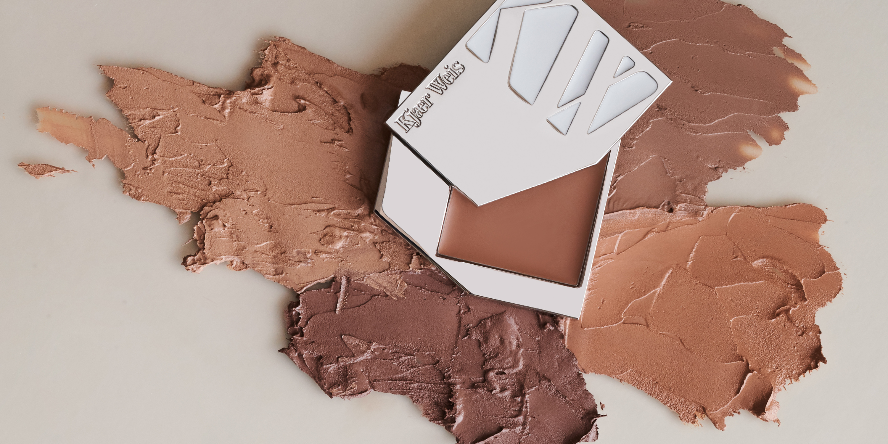 Various swatches of Kjaer Weis Cream Bronzer with Iconic Edition compact on a light background